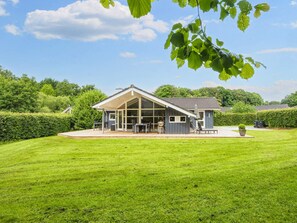 Ein modernes Haus mit einem großen Wintergarten, einer Terrasse und einem gepflegten Rasen.