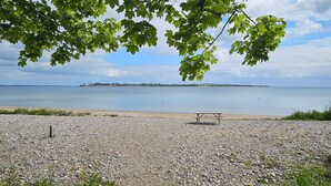Una playa de guijarros con una mesa de picnic y una isla en la distancia.