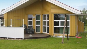 A yellow building with a gabled roof, large windows, and a covered porch with outdoor furniture. - Holiday Home in Otterndorf (Otterndorf)