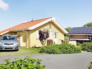 A single-story building with a red-tiled roof, a car parked in front, and a solar panel array to the right.