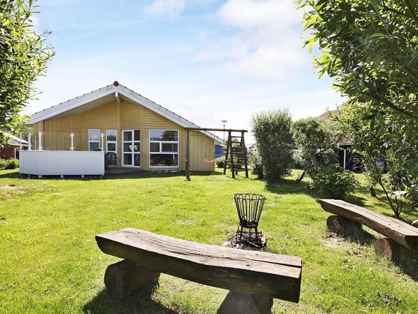 A wooden building with a fenced yard, a wooden bench, and a metal chair.