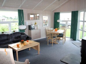 A room with a sofa, a dining table with chairs, a cabinet with a mirror, and a window with curtains.