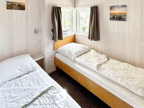 Une chambre avec deux lits simples, une fenêtre avec des rideaux et un tableau accroché au mur.
