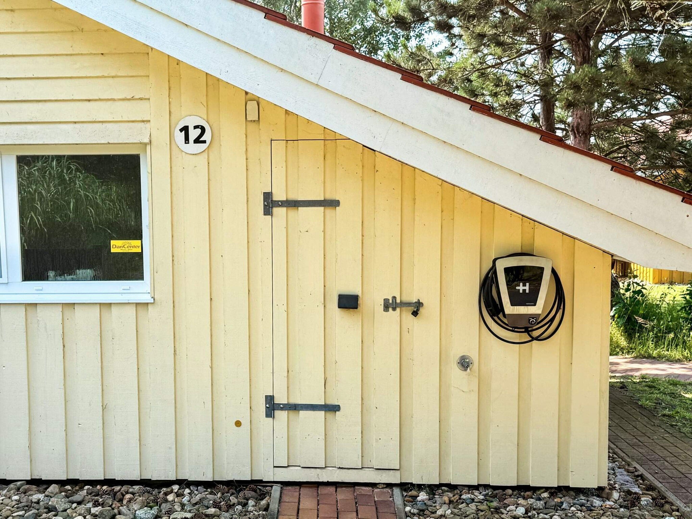 Un edificio giallo con una porta contrassegnata dal numero '12', una finestra e una presa elettrica sulla parete esterna.