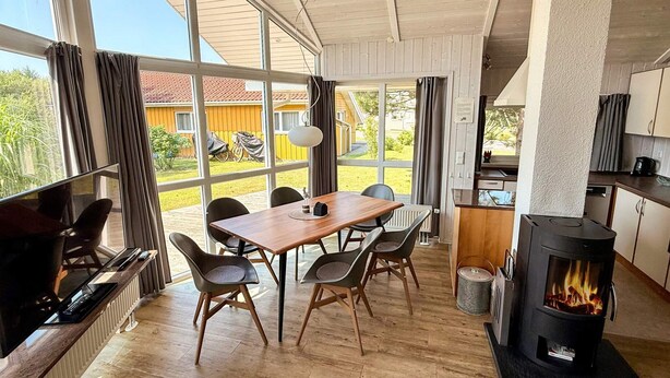 Una cucina moderna con stufa a legna, zona pranzo con tavolo e sedie, e ampie finestre che offrono vista sull'esterno.