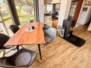 A dining area with a wooden table, grey chairs, and a view of the outdoors through large windows. - Holiday Home in Otterndorf (Otterndorf)