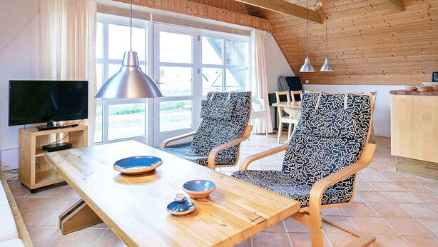A modern living room with a wooden ceiling, a TV on a stand, two patterned chairs, a wooden table with bowls, and a large window. - 6 Person Holiday Home in Ringkobing-by Traum (Ringkobing)