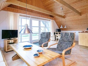 Een moderne woonkamer met een houten plafond, een tv op een standaard, twee gestreepte stoelen, een houten tafel met schalen, en een groot raam.