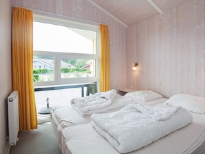 A room with two beds, a window with curtains, a radiator, and a view of houses outside. - Holiday Home in GrÃ¶mmitz (Groemitz)