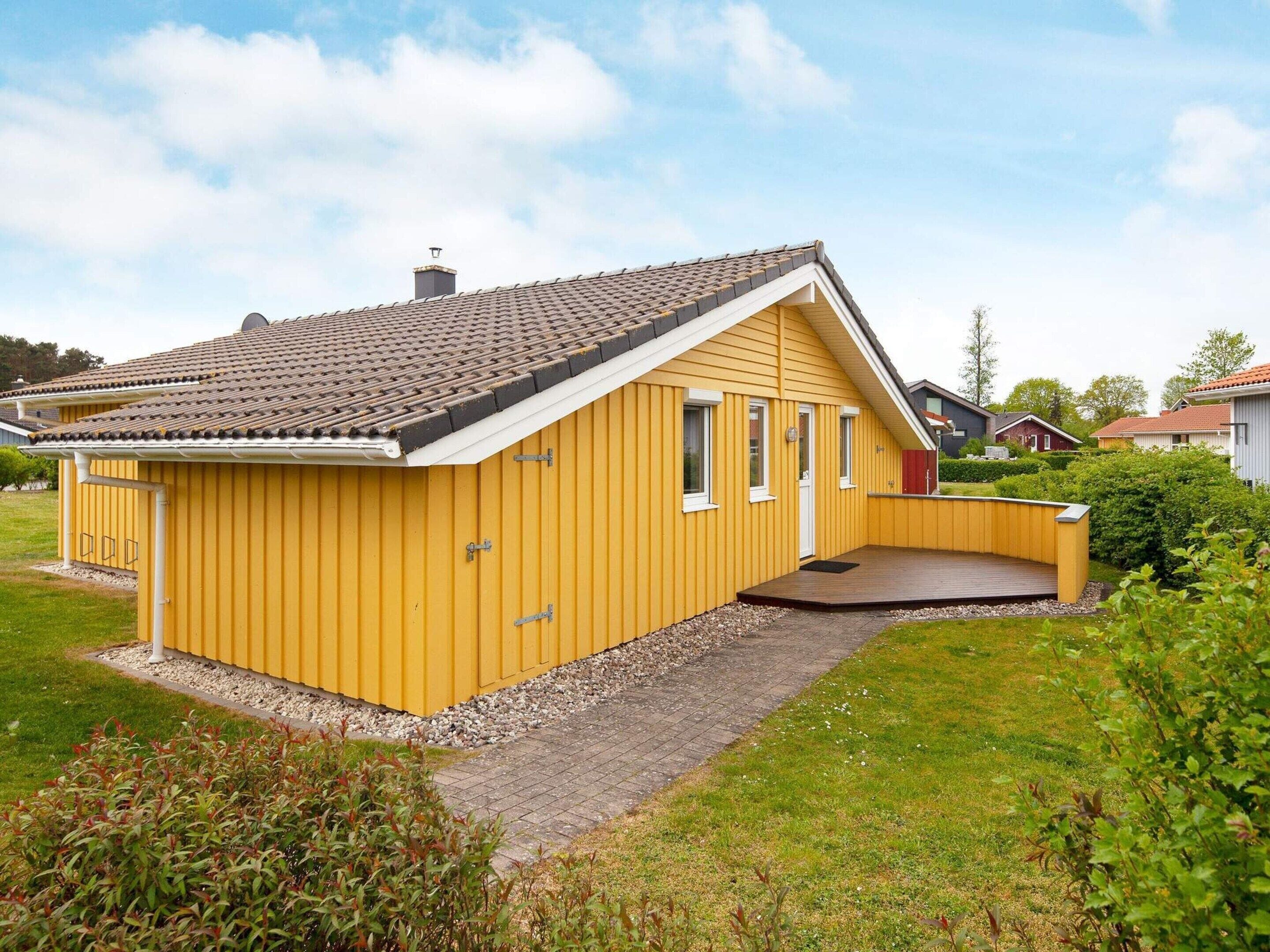A yellow single-story house with a sloped roof, a small porch, and a gravel driveway.