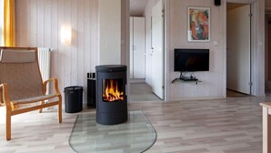 A cozy living room with a wood-burning stove, a comfortable sofa, a television, and a painting on the wall. - Holiday Home in GrÃ¶mmitz (Groemitz)