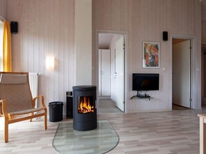 A cozy living room with a wood-burning stove, a comfortable sofa, a television, and a painting on the wall. - Holiday Home in GrÃ¶mmitz (Groemitz)
