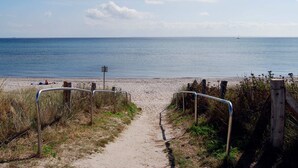 A sandy beach path leading to the sea with a metal railing on one side and a wooden fence on the other.
