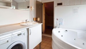 A bathroom with a sink, mirror, washing machine, and a large bathtub.