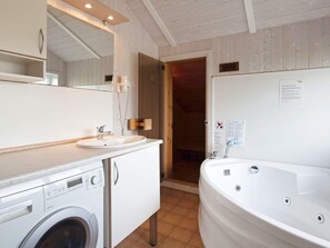 A bathroom with a sink, mirror, washing machine, and a large bathtub. - Holiday Home in GrÃ¶mmitz (Groemitz)