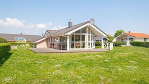 A residential house with a covered patio, a lawn with wildflowers, and neighboring houses.
