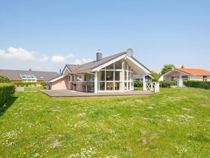 A residential house with a covered patio, a lawn with wildflowers, and neighboring houses. - Holiday Home in GrÃ¶mmitz (Groemitz)