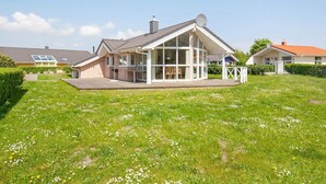 A single-story house with a large glass front, a covered patio, and a well-maintained lawn.