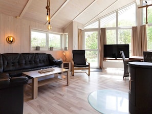 A living room with a black leather sofa, a wooden coffee table, a glass-top table, a black chair, a TV, and large windows with curtains. - Holiday Home in GrÃ¶mmitz (Groemitz)