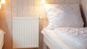 A bedroom with a wooden wall, a radiator, a bed with white bedding, and two wall-mounted lamps. - Holiday Home in GrÃ¶mmitz (Groemitz)