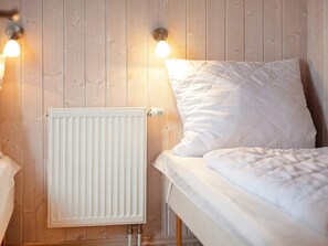 A bedroom with a wooden wall, a radiator, a bed with white bedding, and two wall-mounted lamps. - Holiday Home in GrÃ¶mmitz (Groemitz)