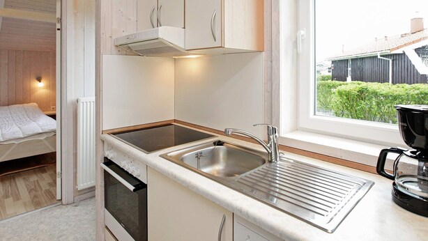 A compact kitchen with a built-in oven, a stainless steel sink, and a window with a view of greenery outside. - Holiday Home in GrÃ¶mmitz (Groemitz)