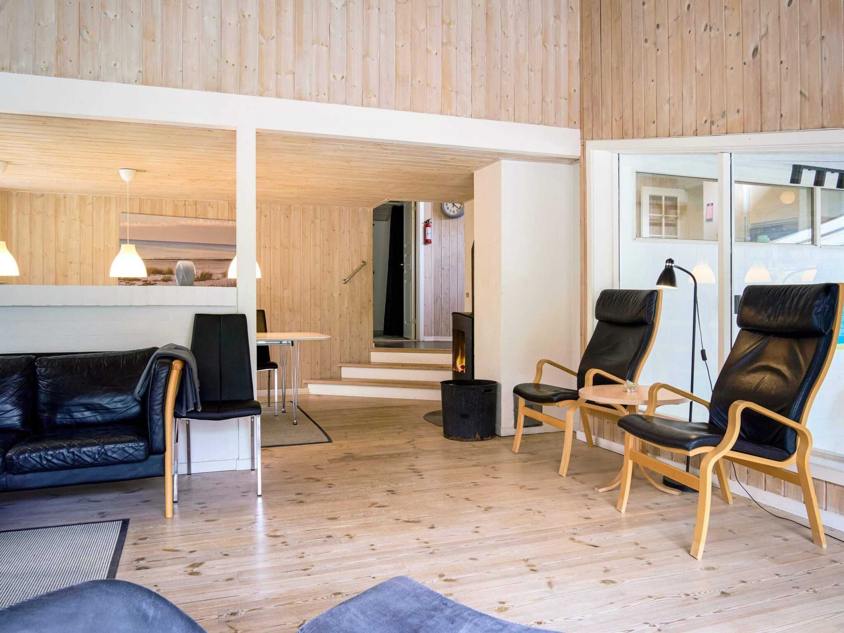 Un interior moderno con techo de madera, un sofá de cuero negro y dos sillones de cuero.