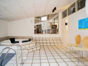 Une piscine intérieure moderne, dotée d’un jacuzzi, d’un sol carrelé et de chaises en bois.