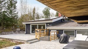 A modern house with a patio area, a covered deck, and a large window.