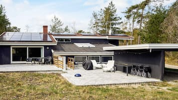 Una casa moderna amb un pati, una zona coberta per seure a l'exterior i un garatge.