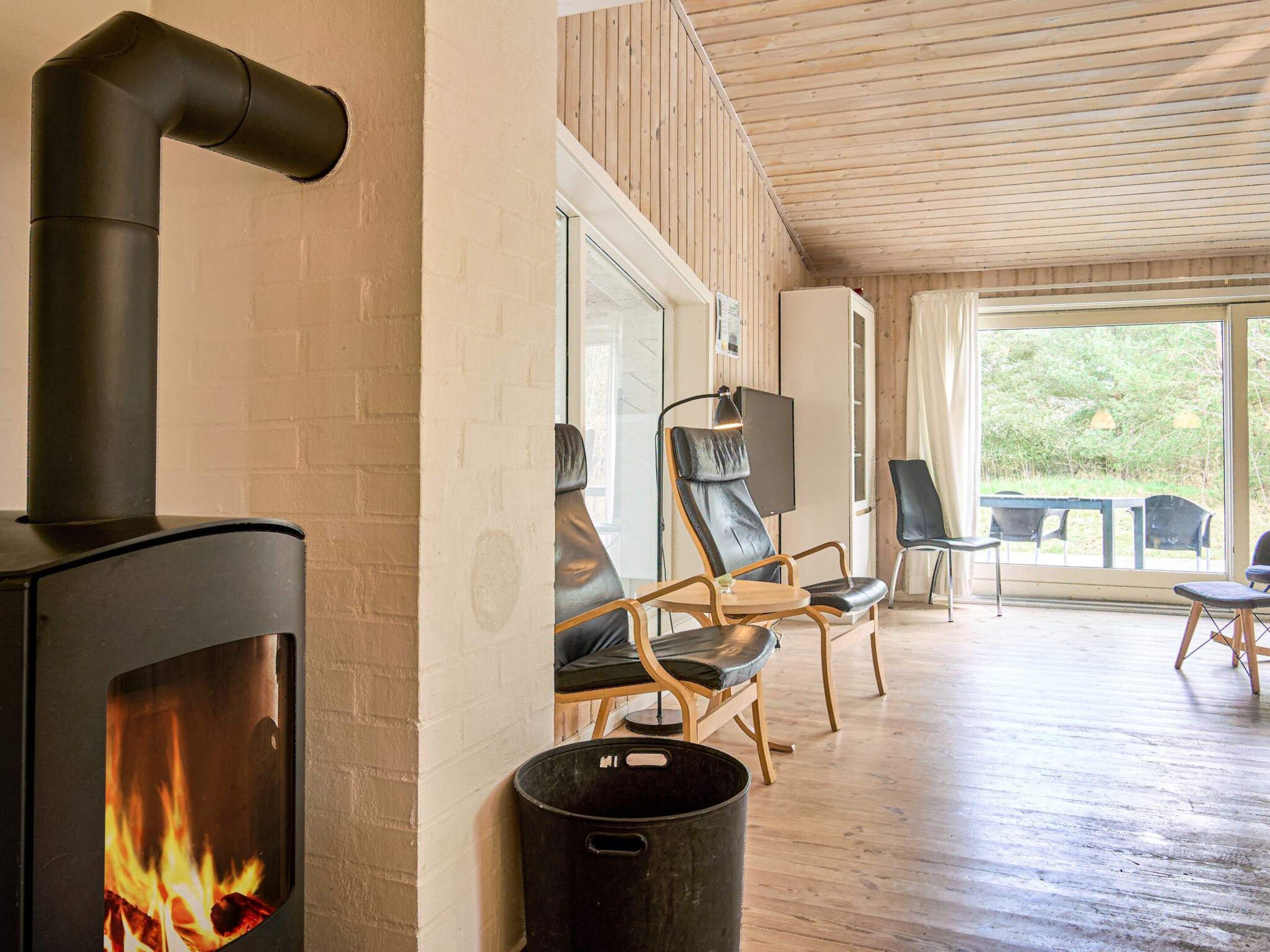 Une pièce chaleureuse avec une cheminée, des murs en bois et une vue sur la verdure environnante.