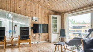 A wooden-paneled room with a flat-screen TV, leather chairs, a small table, and a window with a view of the outside.