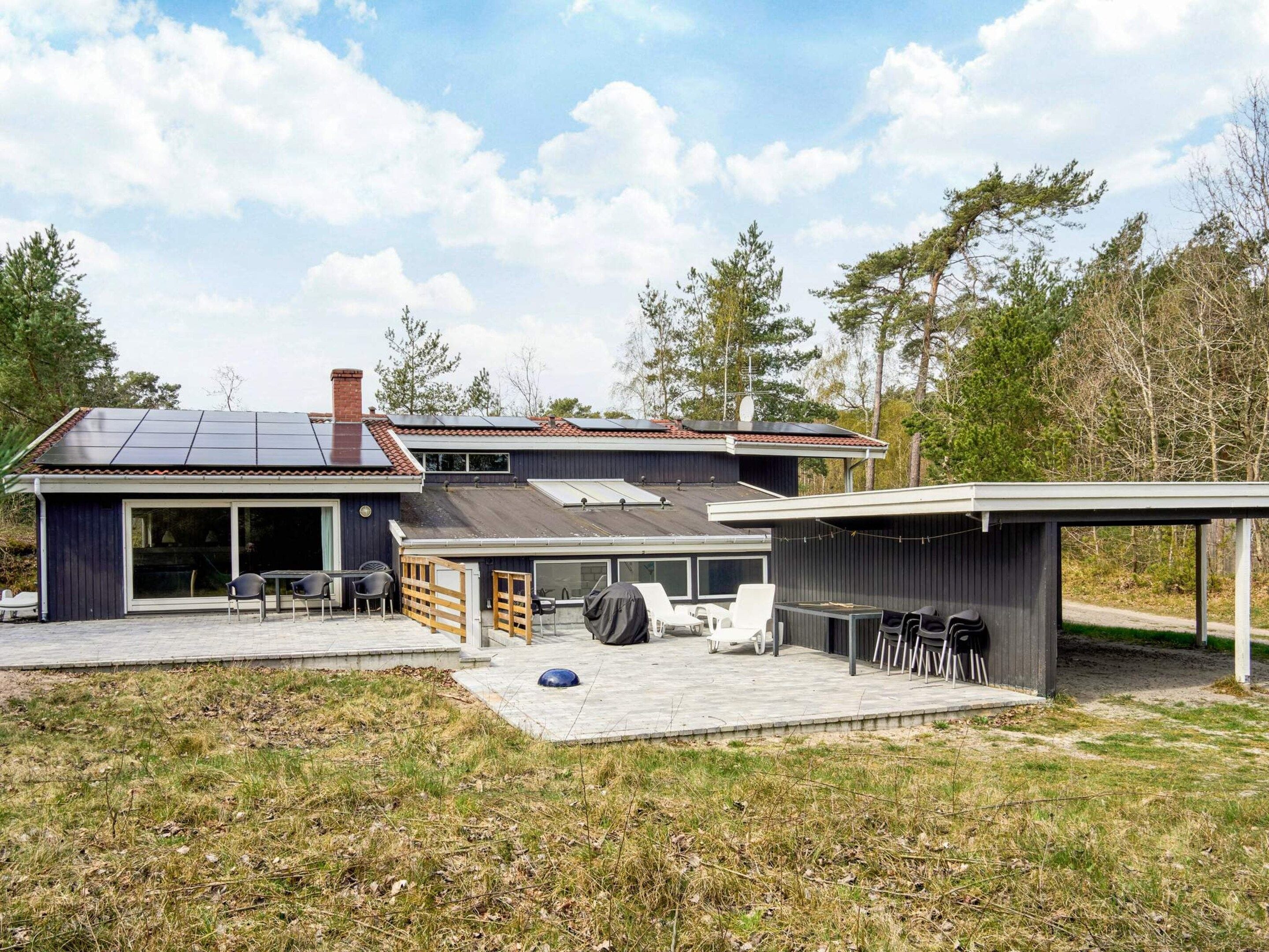Une maison moderne dotée d’un patio couvert, d’un garage et d’un toit équipé de panneaux solaires.