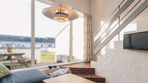 A modern living room with a large window, a wooden table, a sofa, and a television mounted on the wall. - 6 Person Holiday Home in Brovst-by Traum (Brovst)