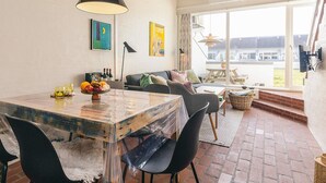 A dining area with a rustic wooden table, black chairs, and a clear plastic cover. There are two paintings on the wall, a black pendant light, and a view of the outside through large windows. - 6 Person Holiday Home in Brovst-by Traum (Brovst)