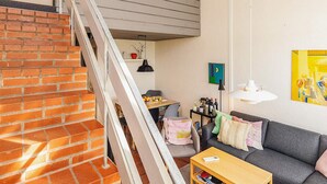 A staircase leading to a loft area with a brick wall, a gray sofa, and a table with books. - 6 Person Holiday Home in Brovst-by Traum (Brovst)