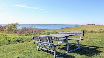 A picnic table and bench in a grassy field with a view of the sea.