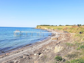 A beach with a wooden pier extending into the water, a picnic table, and a grassy area with a person in the distance. - Spacious Holiday Home in TranekÃ¦r near Sea (Tranekaer)