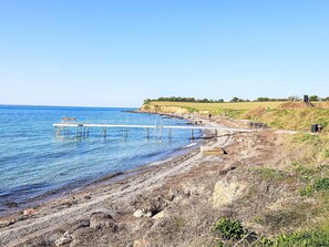 A beach with a wooden pier extending into the water, a picnic table, and a grassy area with a person in the distance. - Spacious Holiday Home in TranekÃ¦r near Sea (Tranekaer)