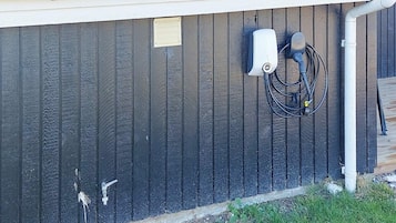 A building exterior with a dark vertical siding, a small utility box, and a hose connected to a water source.