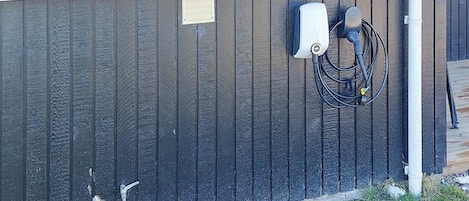 A building exterior with a dark vertical siding, a small utility box, and a hose connected to a water source.