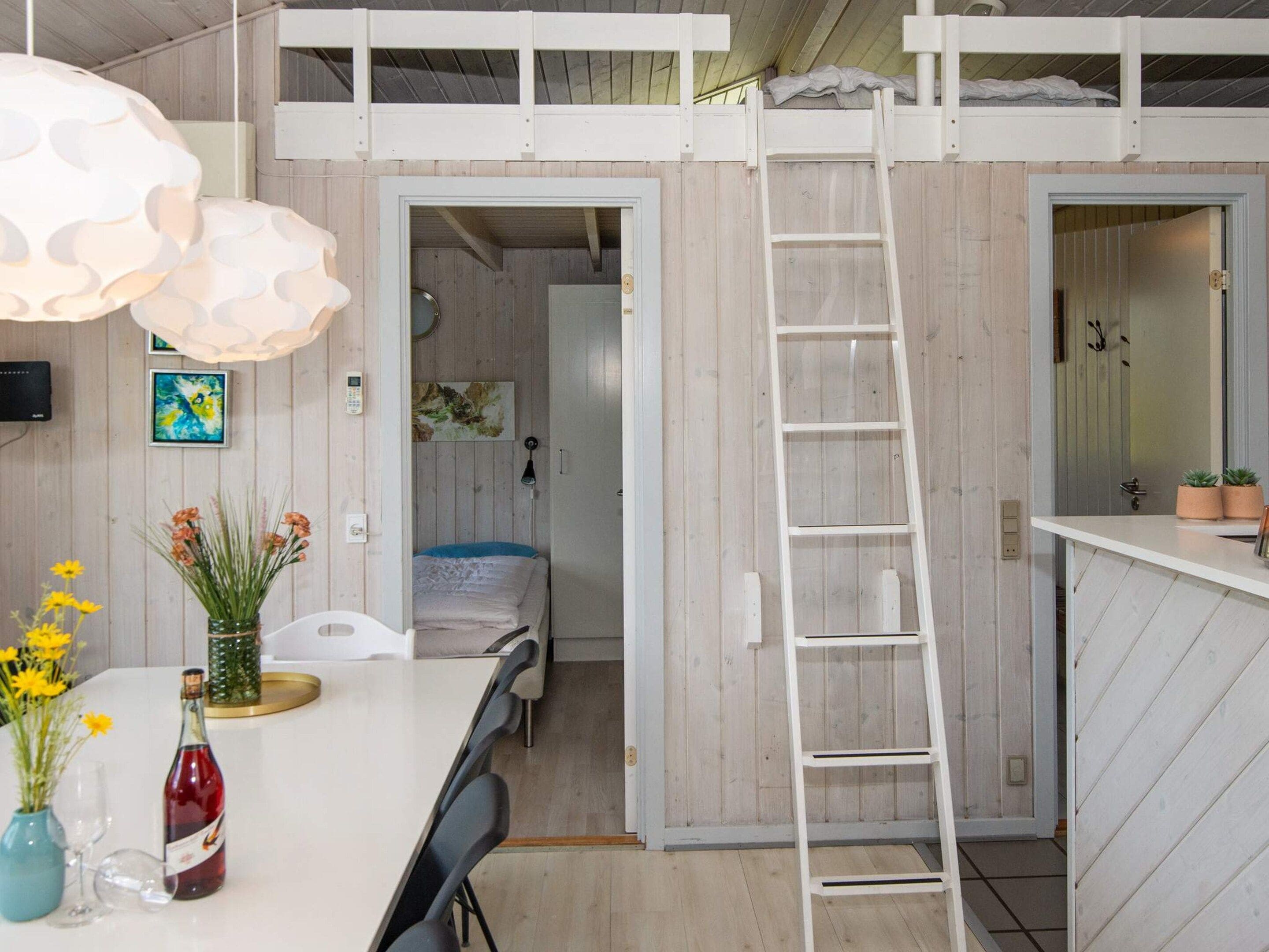Une pièce compacte comprenant un lit superposé, une échelle, un coin repas avec une table et des chaises, et une kitchenette.