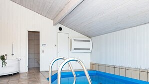 An indoor swimming pool with a tiled floor, a white wall with a door, and a white ceiling.