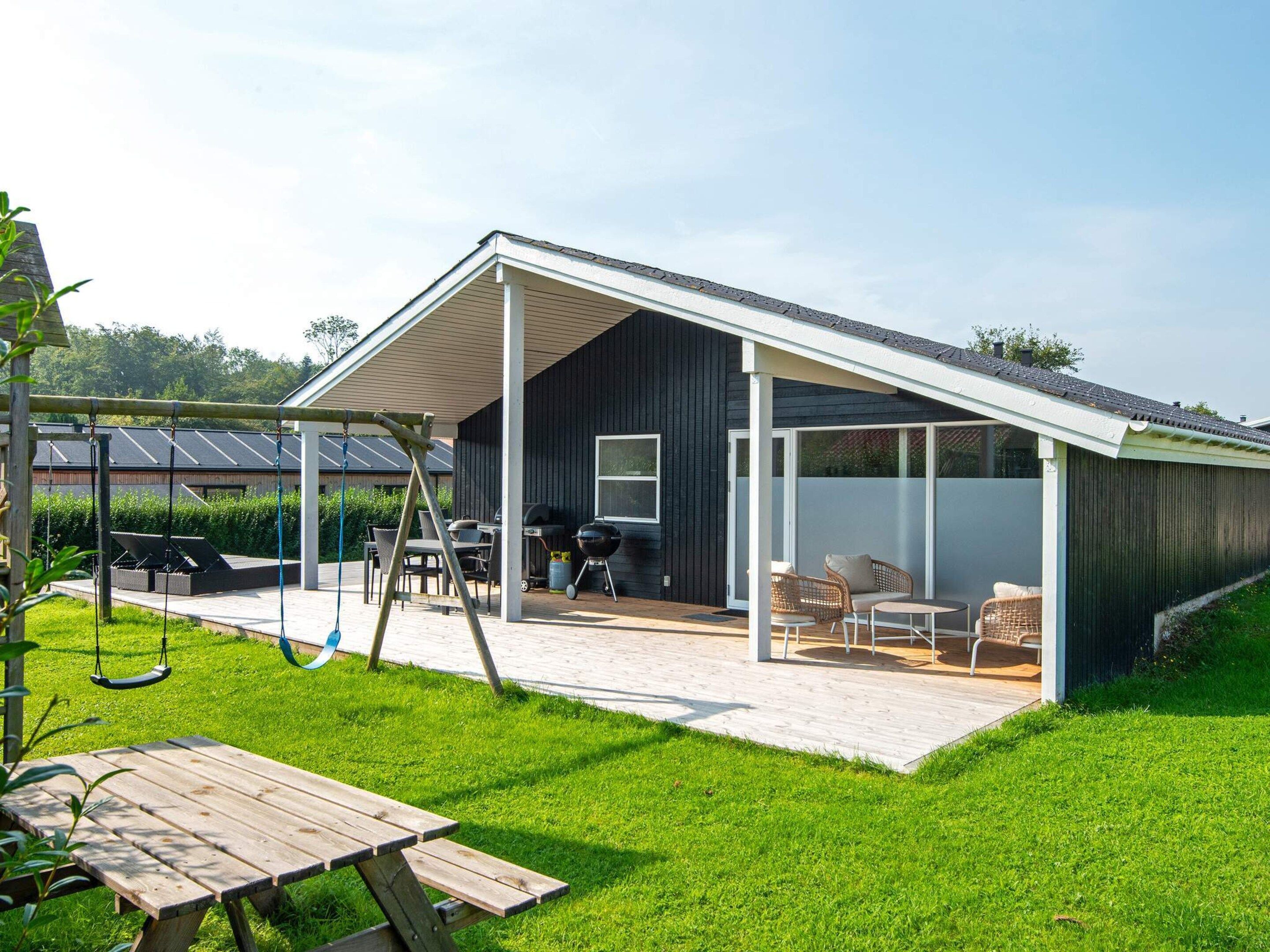 Una casa moderna con un patio cubierto, mobiliario exterior y un columpio.