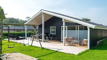 Una casa moderna con un patio cubierto, mobiliario exterior y un columpio.