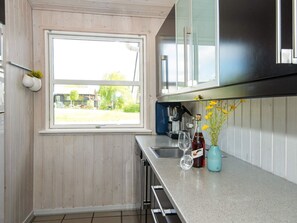Et køkken med et vindue, rustfrie apparater og en vase med blomster på bordpladen.