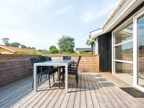 En træterrasse med et bord, stole, en glasdør og udsigt over kvarteret.