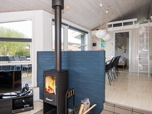 A modern living room with a wood-burning stove, a TV, and a dining area with chairs and a table.