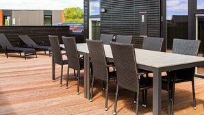 An outdoor dining area with a table and chairs, a grill, and a modern building facade. - Stylish Holiday Home in Jutland near Baltic Sea Beach (Hadsund)
