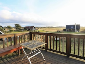 A wooden deck with a metal table and bench, overlooking a grassy landscape with buildings.